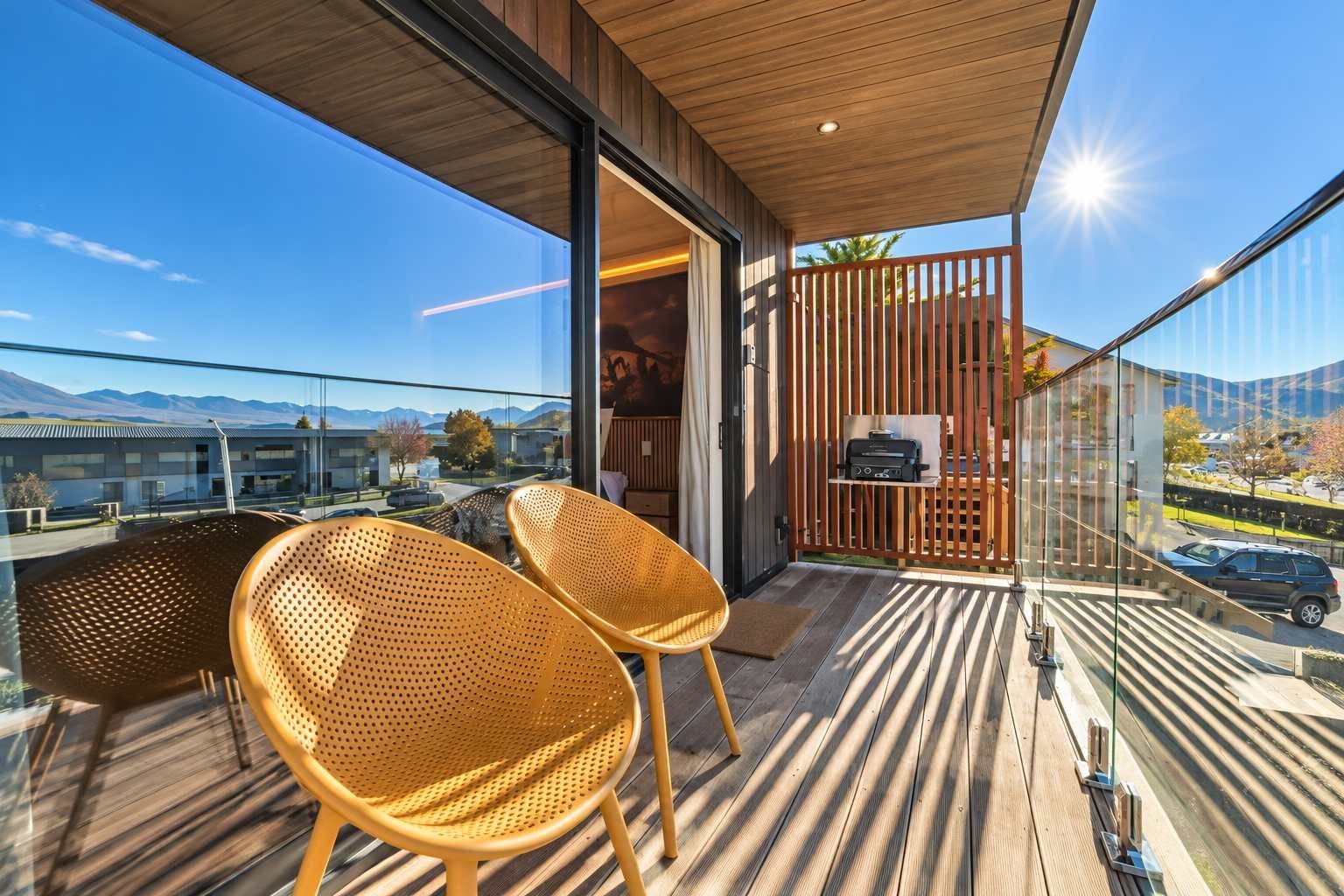 A balcony with two wicker chairs, a wooden floor, and a view of a cityscape and mountains.