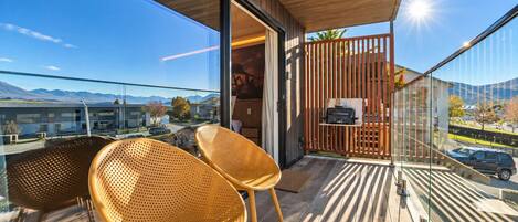 A balcony with two wicker chairs, a wooden floor, and a view of a cityscape and mountains.