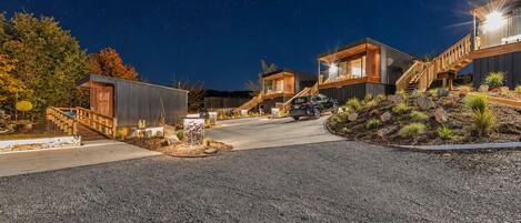 A modern residential area with multiple houses connected by a pathway, featuring a gravel driveway and landscaped areas.