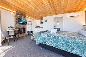 Une chambre d’hôtel moderne équipée d’un lit, d’un coin salon et d’un téléviseur fixé au mur, qui est en pierre.