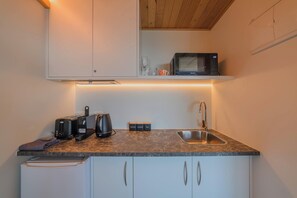 A compact kitchen with a microwave, toaster, kettle, and a coffee maker on the counter. - Starlight Escape - Ohana (Lake Tekapo)