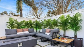 A modern outdoor seating area with a grey sectional sofa, a wooden coffee table, and potted plants. - Heated Pool • Games • Fire Pit • BBQ • Sleeps 12 (Bradenton)