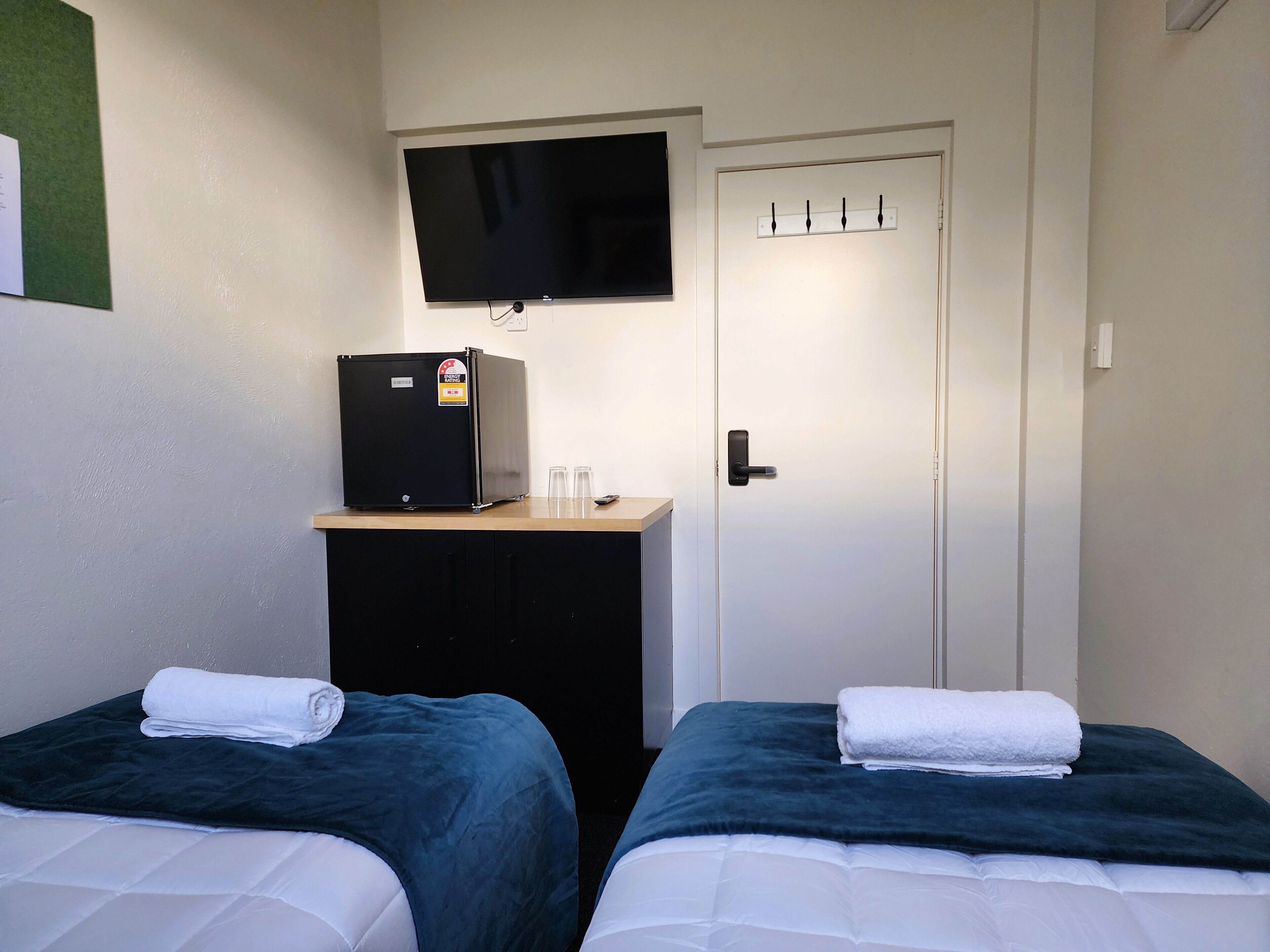 A hotel room with two beds, a television, a minibar, and a door with a lock.