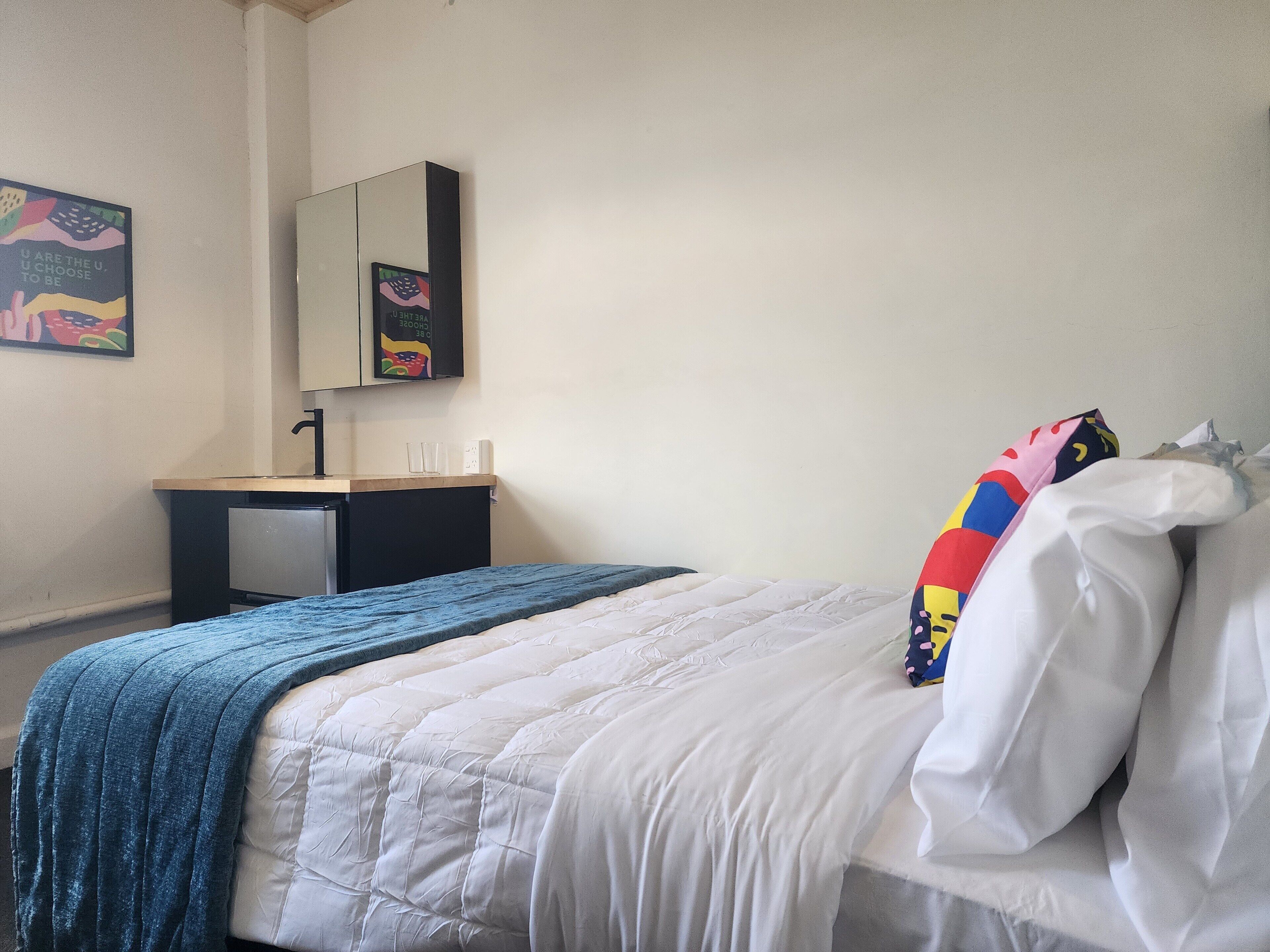 A bedroom with a bed, a bedside table, a mirror, and a wall with a poster.