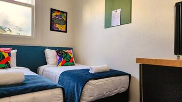 A hotel room with two beds, a window, a bulletin board, and a desk.