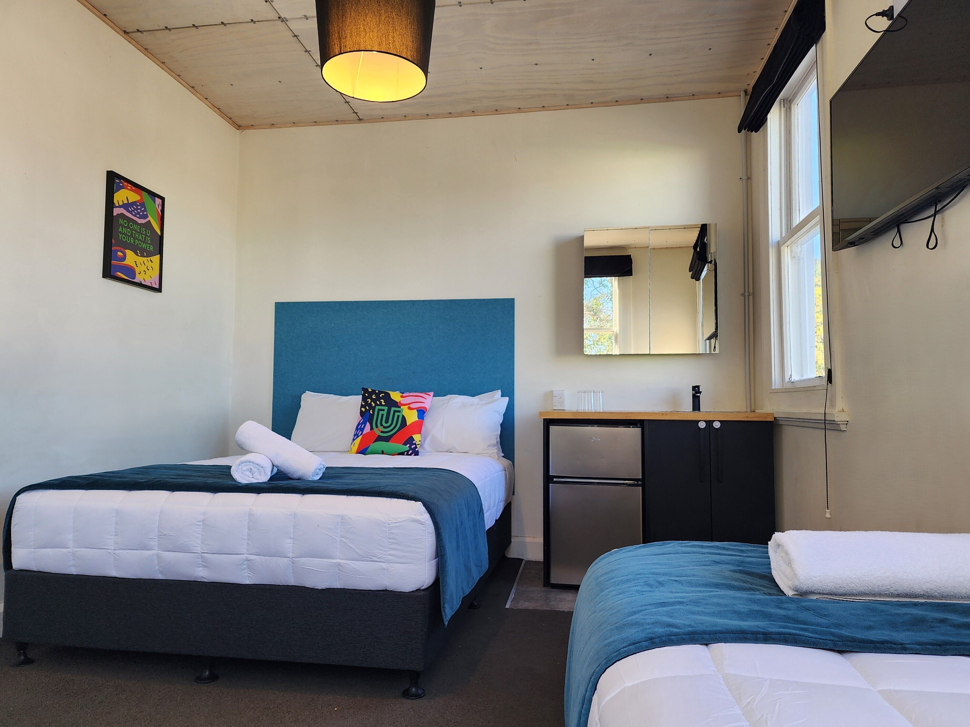 Een hotelkamer met twee bedden, een klein bureau, een spiegel en een plafondlamp.