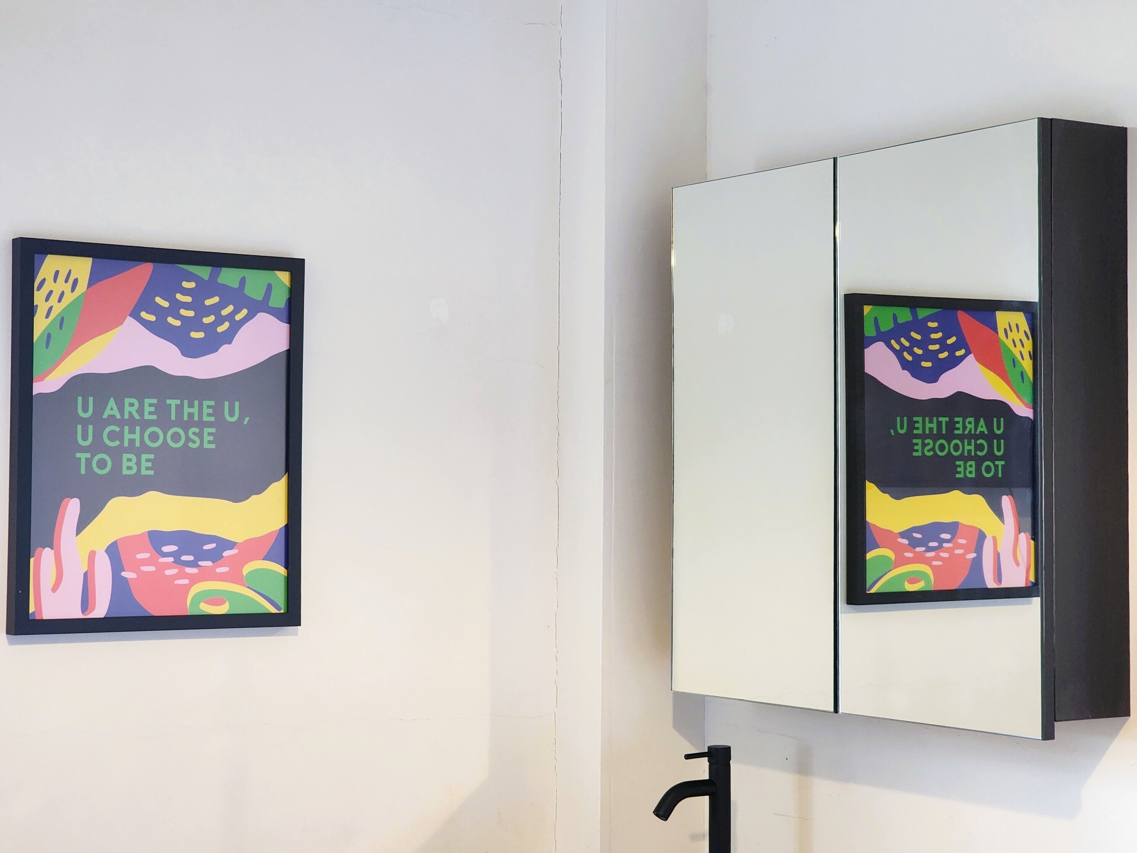 A wall with two framed posters and a mirrored cabinet.