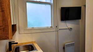 Une cuisine équipée d’un évier en acier inoxydable, d’une fenêtre, d’un téléviseur fixé au mur et d’un radiateur encastré.