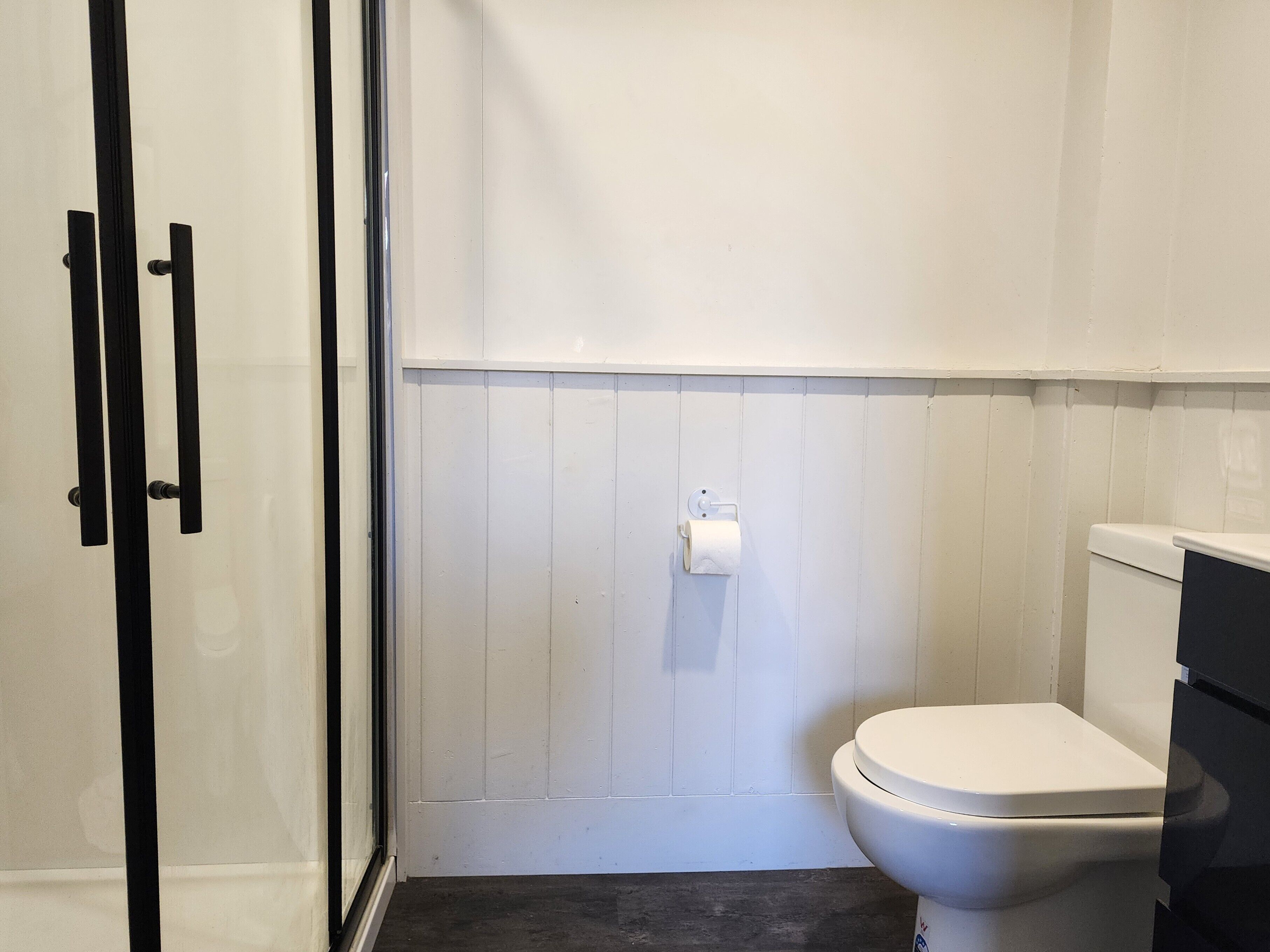 A bathroom with a white toilet, a paper towel dispenser, and a glass shower enclosure.
