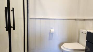 A bathroom with a white toilet, a paper towel dispenser, and a glass shower enclosure.