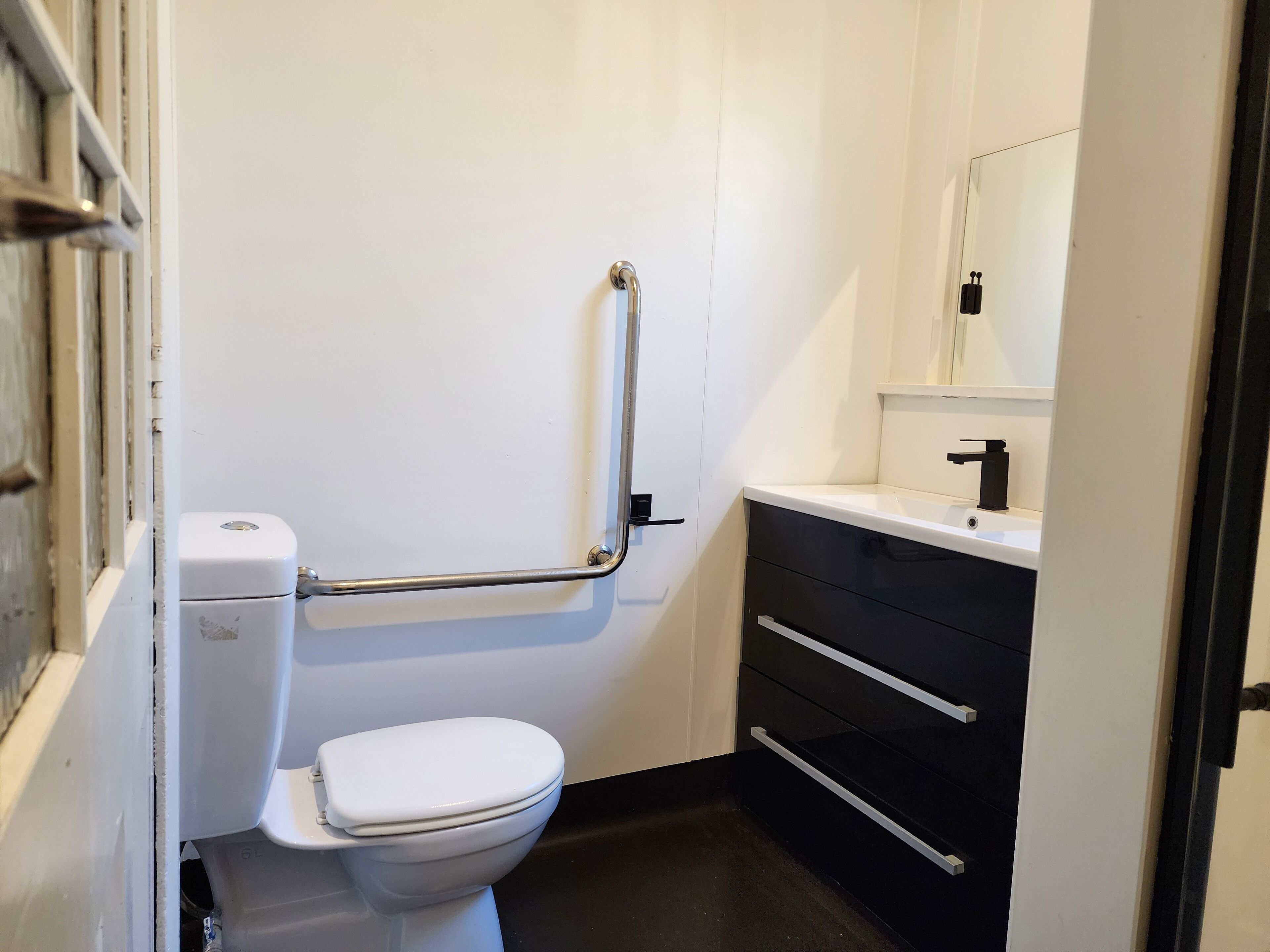 Un baño con inodoro blanco, lavamanos negro y un espejo sobre el lavamanos.