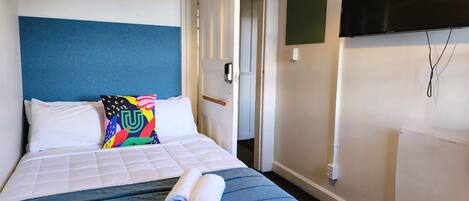 A hotel room with a bed, a colorful pillow, a TV, and a door.