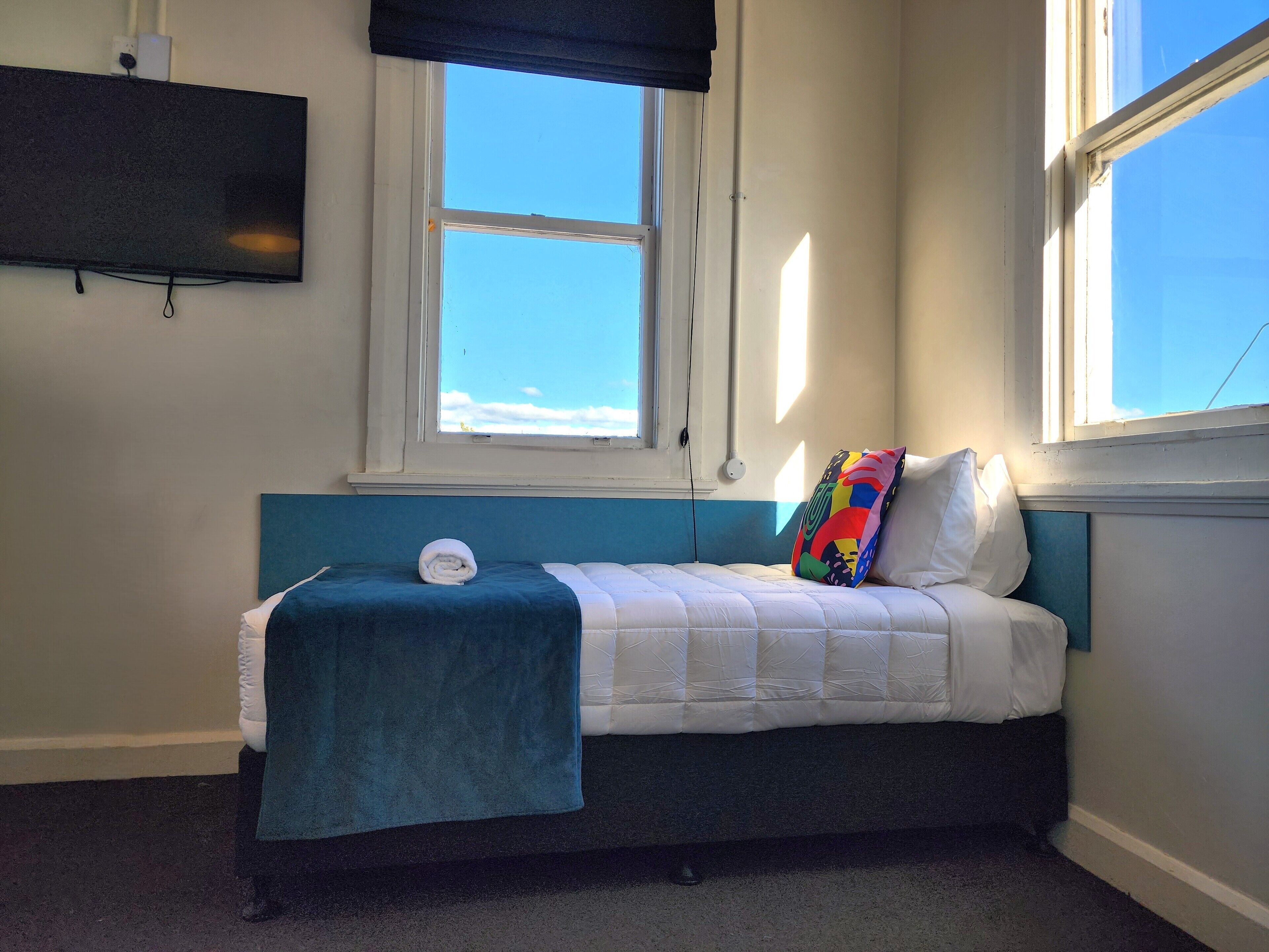 A bedroom with a bed, a TV mounted on the wall, and a window with a view of the sky.