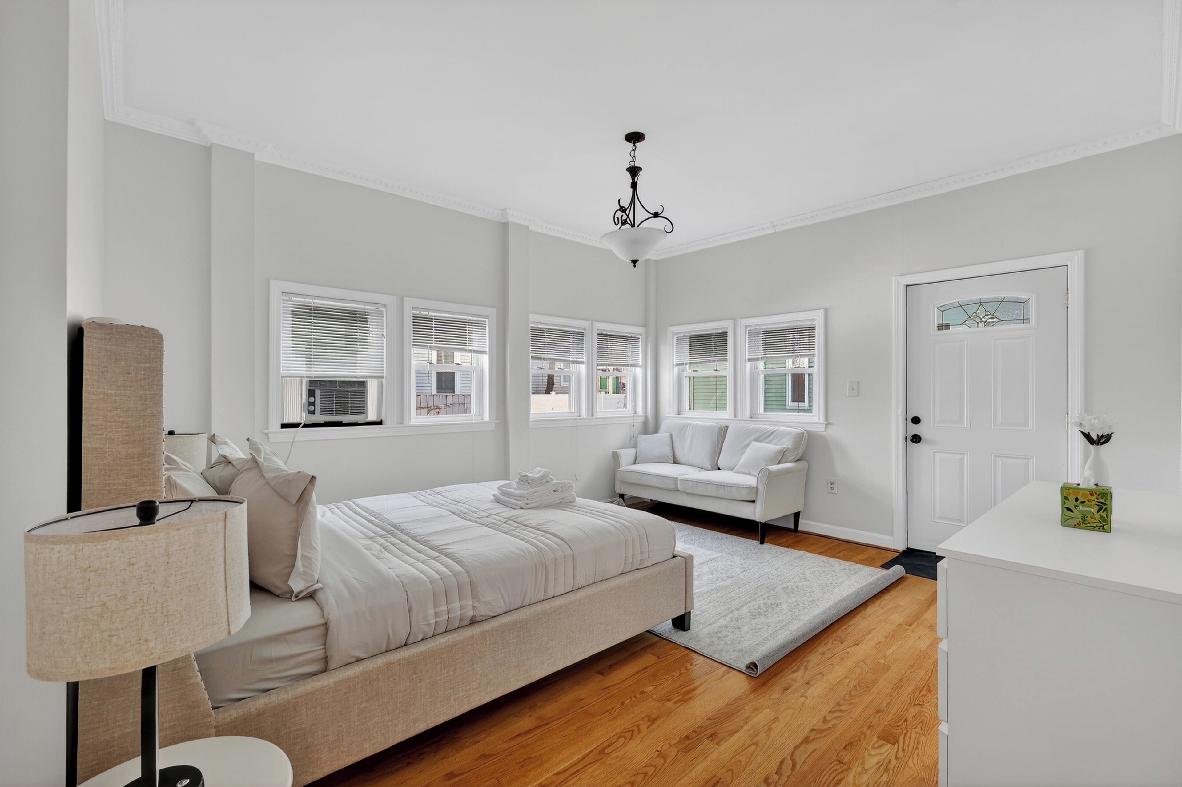 A bedroom with a bed, a bedside table, a lamp, a sofa, and a door.