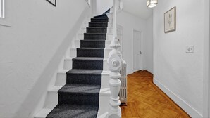 A staircase with dark carpeted steps and white railings, leading to a door with a radiator on the wall. - Cozy&Spacious 7Br home in Malden + free Parking (Malden)
