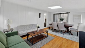 A modern living room with a grey sofa, a wooden coffee table, and a dining area with a table and chairs. - Cozy&Spacious 7Br home in Malden + free Parking (Malden)