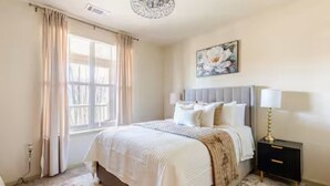 Una camera da letto con un letto, tende, un comodino, una lampada e un quadro appeso al muro.