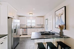 A modern kitchen with white cabinets, stainless steel appliances, a marble countertop, and a bar stool. - 3ksqft | PetsOK | Mountain View| The Bondline Home (Sheridan)