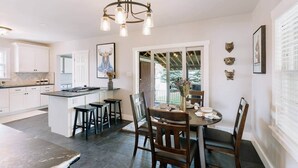 Een moderne keuken met witte kastjes, een centraal kookeiland, barstoelen en een eethoek met tafel en stoelen.
