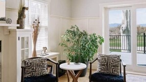 Een kamer met twee stoelen, een klein tafeltje, een plant en uitzicht door een groot raam.
