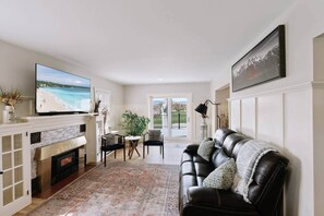 A living room with a fireplace, a television, a couch, and a view of the outdoors. - 3ksqft | PetsOK | Mountain View| The Bondline Home (Sheridan)