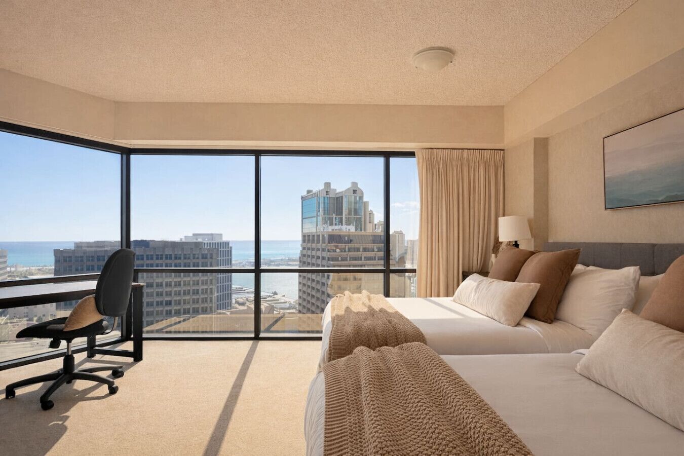 A hotel room with a large window, a bed, a desk, and a chair.