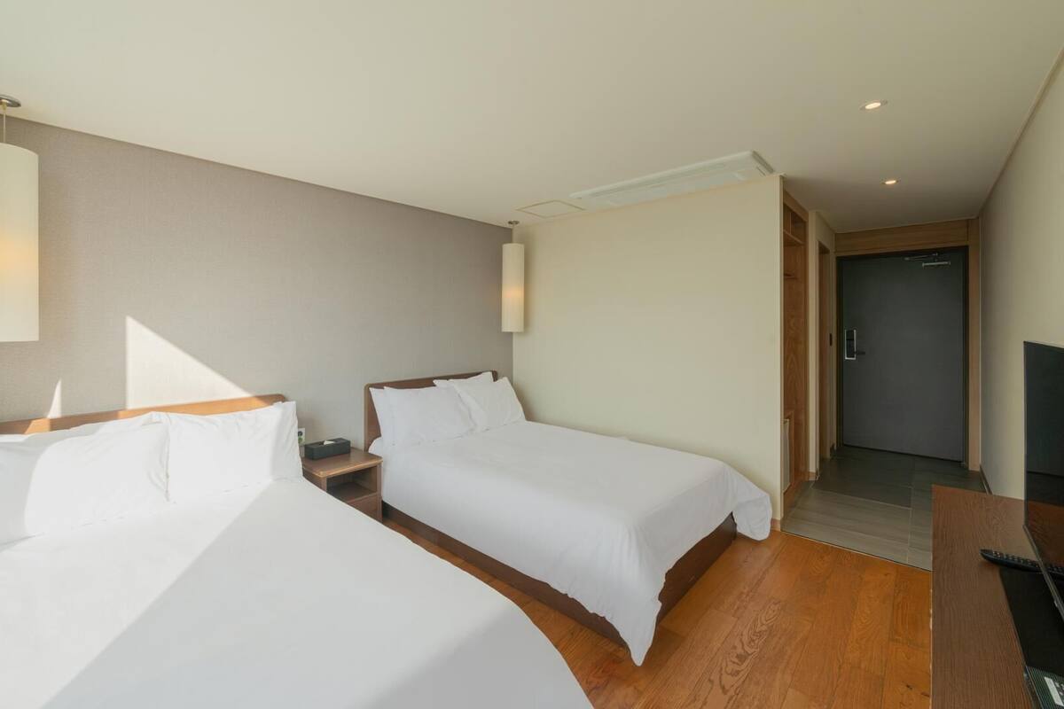 A hotel room with two beds, a TV, and a door leading to a bathroom.