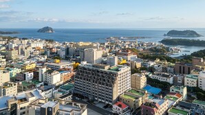 Zona urbana densamente construida, con una mezcla de edificios residenciales y comerciales, un rascacielos destacado y vistas al mar con islas en la distancia.