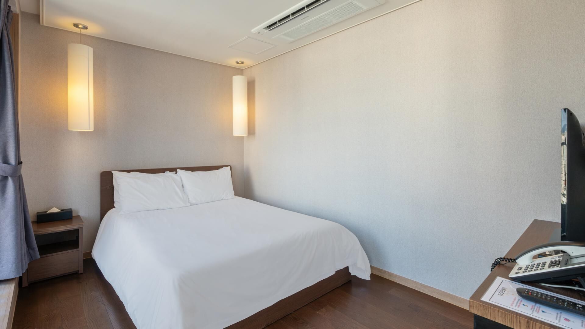 A hotel room with a bed, bedside table, lamp, TV, and a telephone.