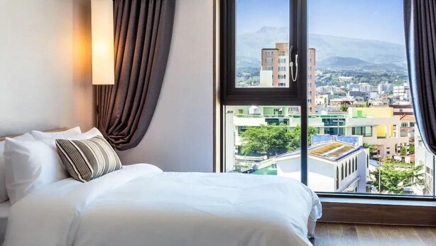 Habitación de hotel con una cama grande, vistas a la ciudad y una ventana con cortinas.