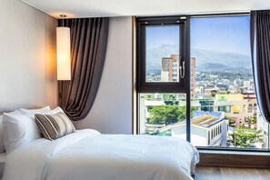 A hotel room with a large bed, a view of a cityscape, and a window with curtains. - Temata Hotel Seogwipo Jeju (Seogwipo)