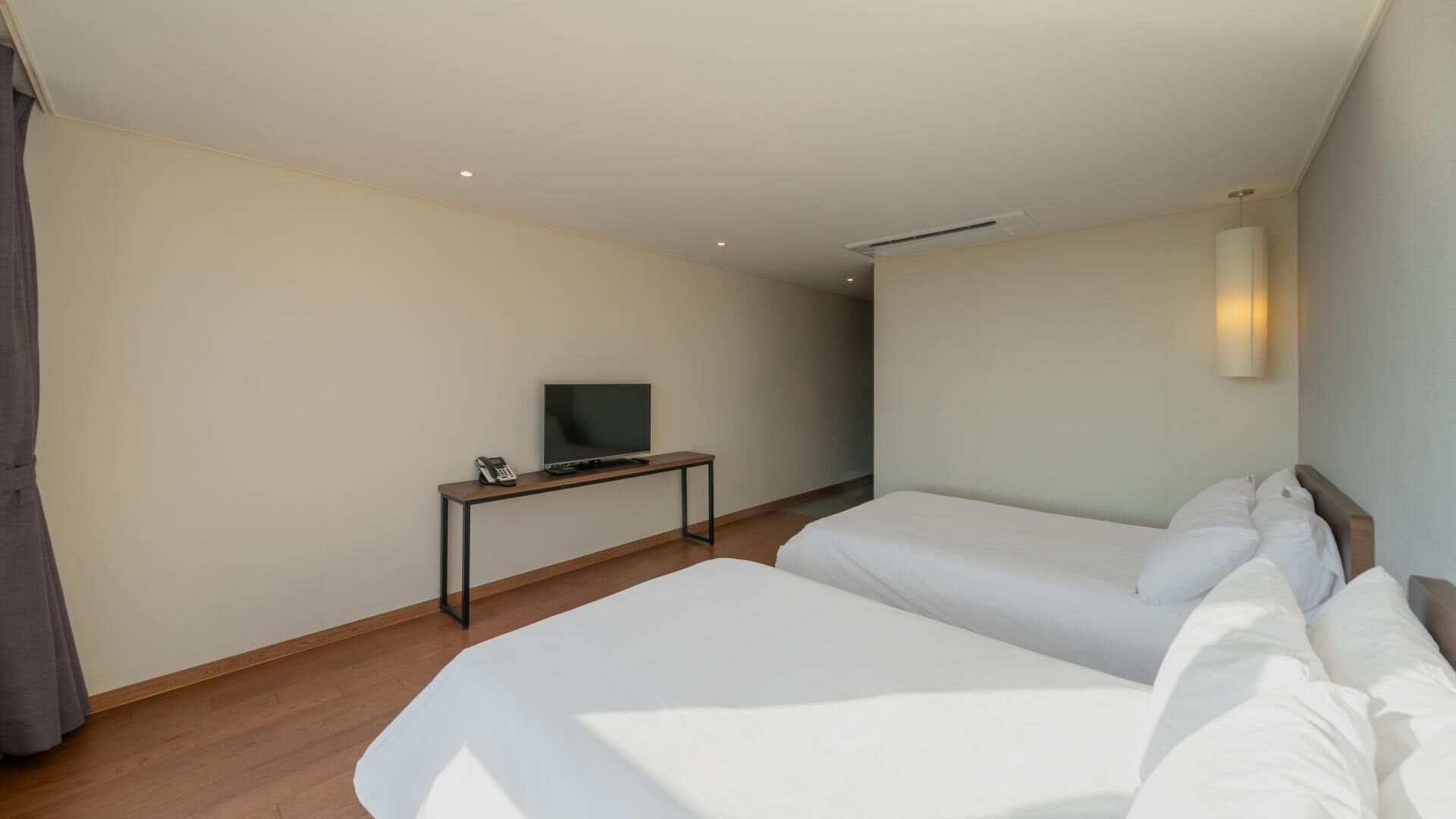 Une chambre d’hôtel avec deux lits, un téléviseur posé sur un bureau et une lampe fixée au mur.
