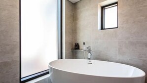Un baño moderno con una bañera independiente, un ventanal y un estante pequeño con artículos de aseo.