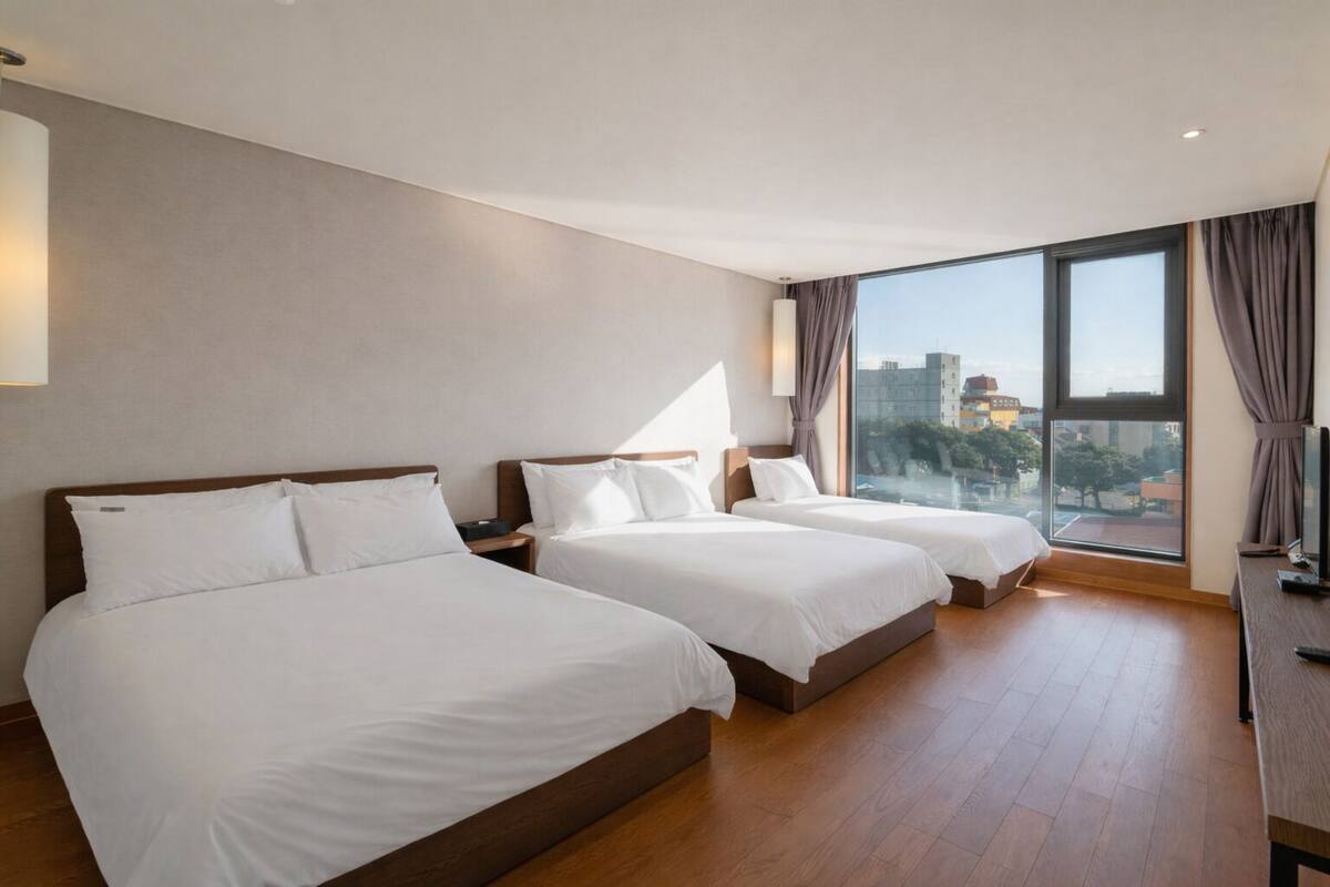 A hotel room with two beds, a large window with a city view, and a desk with a computer.