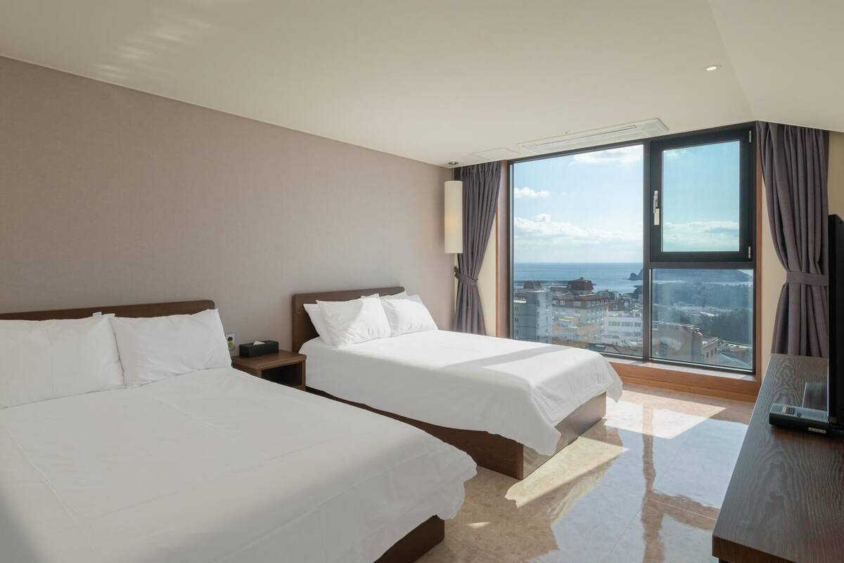 A hotel room with two beds, a large window with a city view, and a modern design.