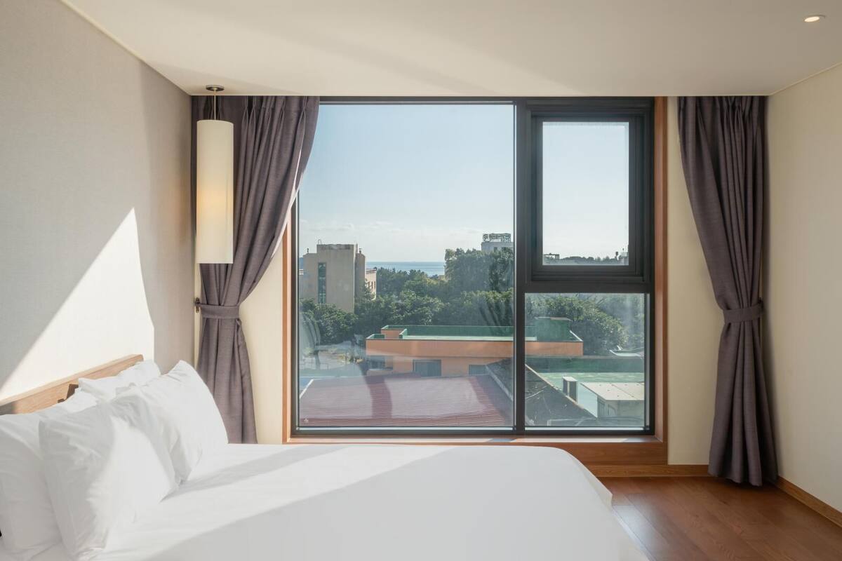 A hotel room with a large bed, a view of the cityscape, and a window with curtains.