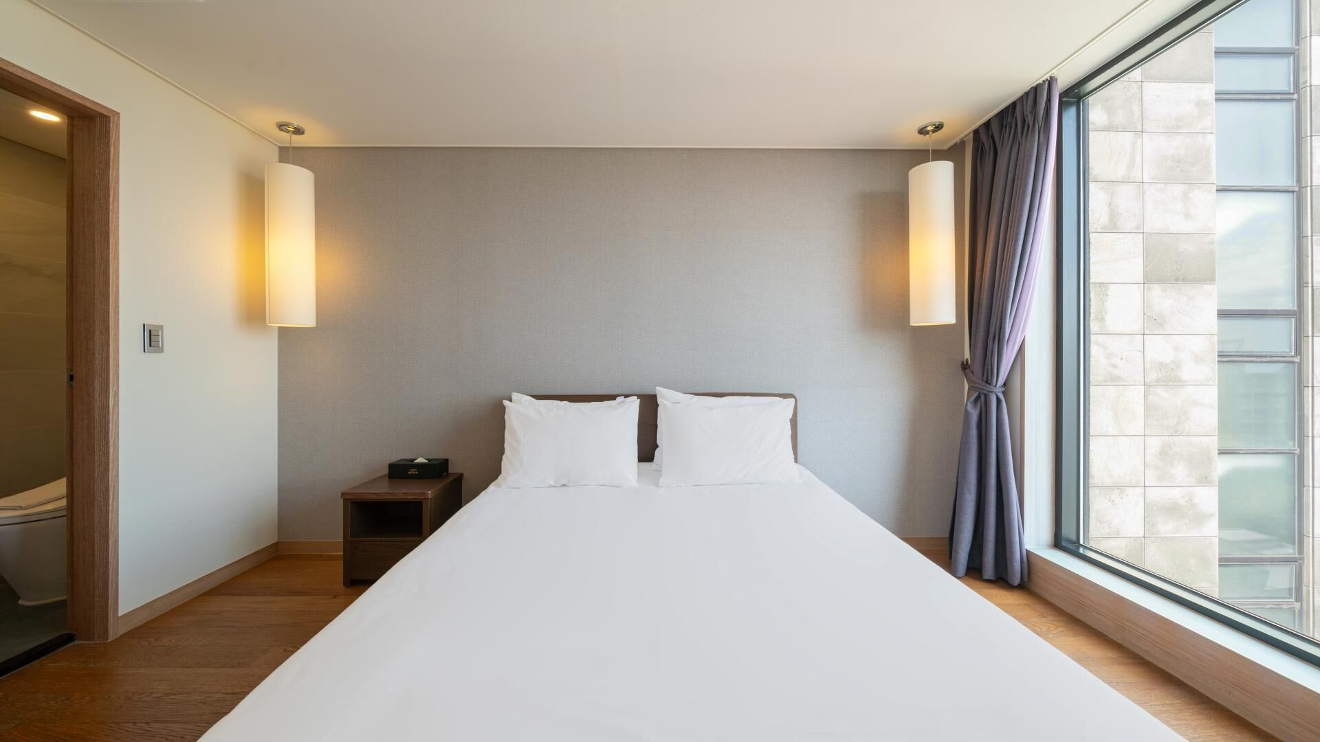 A hotel room with a large bed, bedside lamps, a nightstand, and a window with curtains.