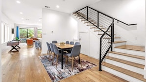 Un salon moderne avec un plancher en bois, un coin repas comprenant une table et des chaises, un canapé et un escalier doté d’une rampe noire.