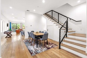 Un salon moderne avec un plancher en bois, un coin repas comprenant une table et des chaises, un canapé et un escalier doté d’une rampe noire.