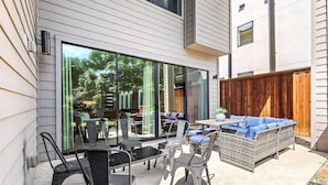 Une terrasse aménagée avec du mobilier d’extérieur, notamment un canapé et des fauteuils en osier, et une porte vitrée donnant sur un jardin.