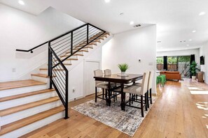 A modern interior with a wooden staircase, a dining area with a table and chairs, and a sofa in a bright room with large windows. - Captive Comfort Downtown, Mkt Ctr, Garage, DART! (Dallas)