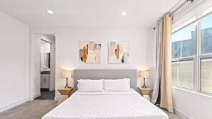 Een moderne slaapkamer met een groot bed, twee nachtkastjes en abstracte wanddecoratie.