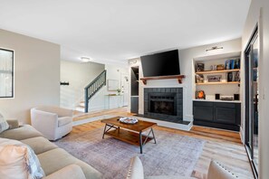 A modern living room with a fireplace, a sofa, a coffee table, and a staircase leading to another level. - 202 Beachwalk 3BR/3.5BA Villa 10min Walk to Beach (Hilton Head Island)