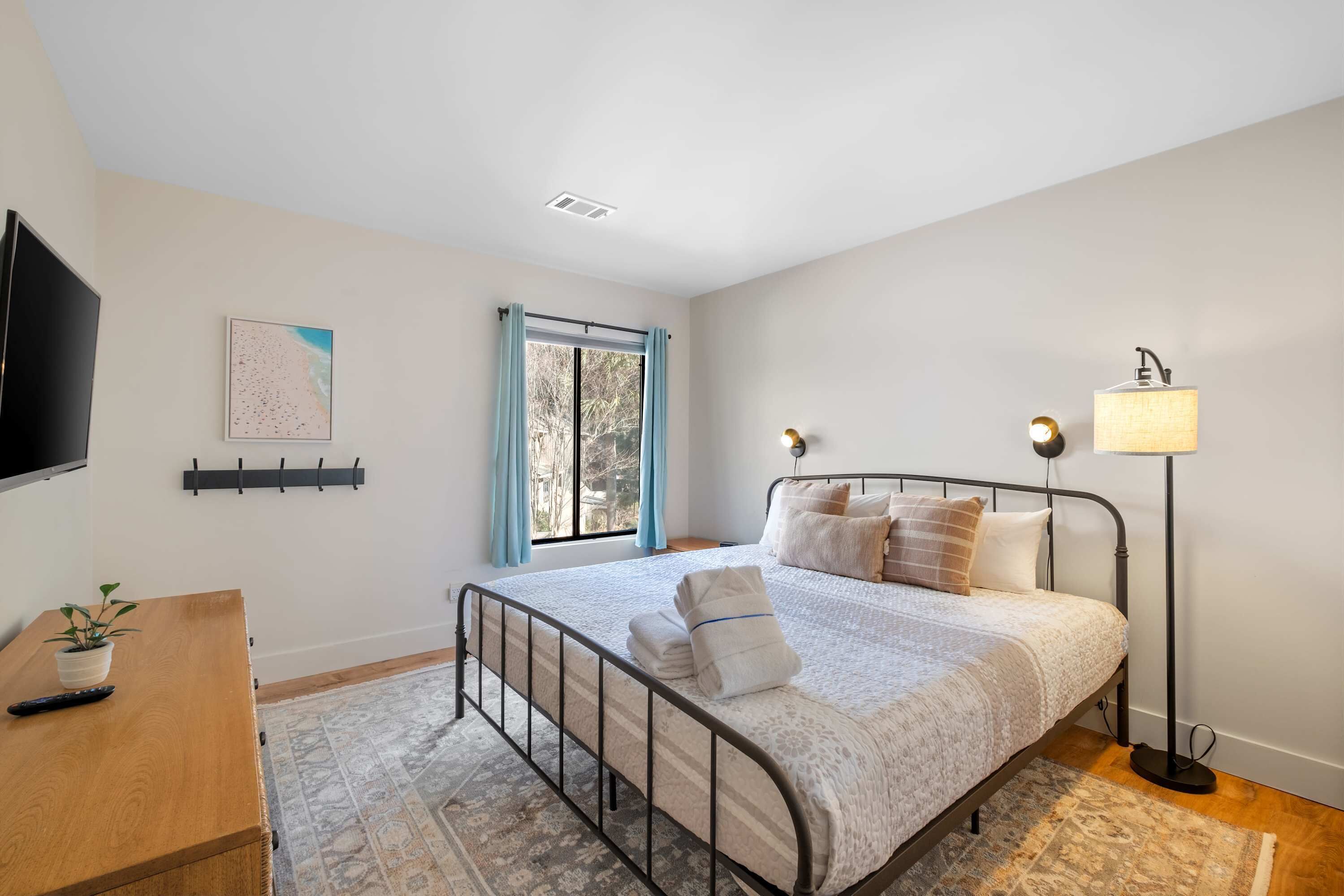 A bedroom with a bed, bedside lamp, and a TV on a wooden dresser.