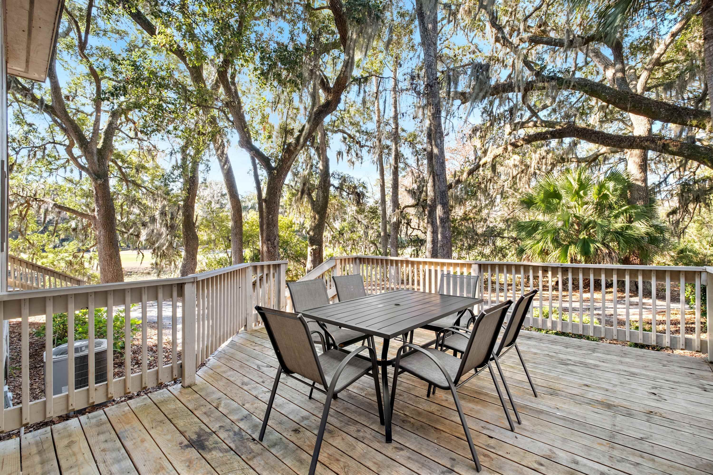 A wooden deck with a table and chairs, surrounded by trees and a white fence.
