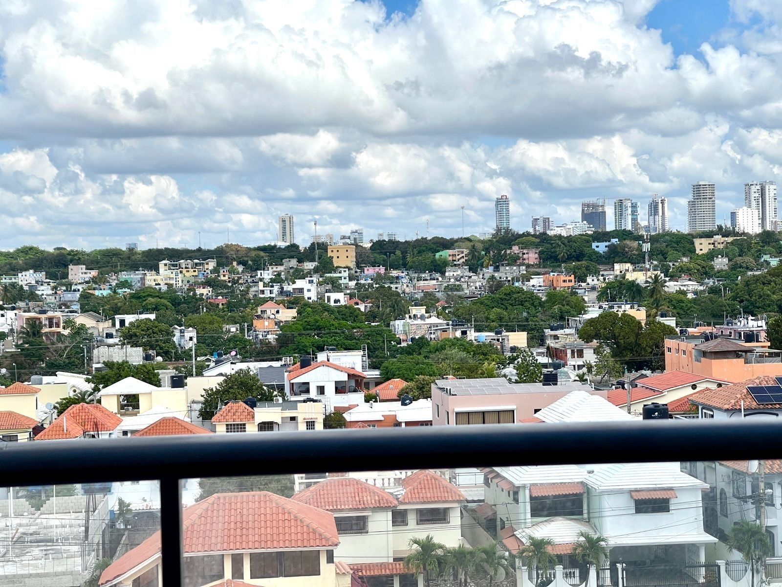 A residential area with a variety of houses, some with red-tiled roofs, and a distant view of a city skyline with tall buildings.