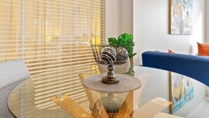 Una sala de estar moderna con una mesa de vidrio, un cuenco decorativo de metal, una planta en maceta y un sofá azul.