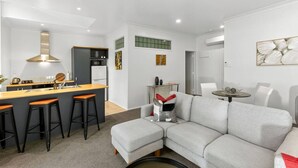 A modern kitchen with a central island, bar stools, a grey sofa, and a dining table. - Heart of Hamilton Loft – Light, Luxury & Location (Hamilton)