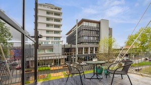 A balcony with outdoor furniture, a view of a modern building, and a clear sky. - Heart of Hamilton Loft – Light, Luxury & Location (Hamilton)