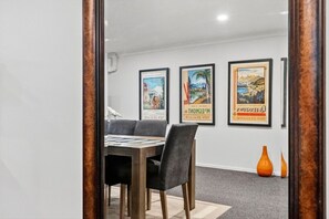 A dining area with a table and chairs, framed travel posters on the wall, and a vase on the floor. - Upmarket- Heart of Hamilton Apt (Hamilton)